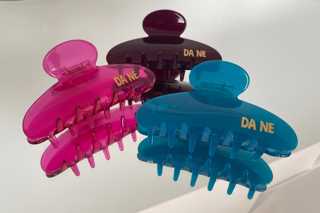 Three colorful hair clips with 'DA NE' branding on a light background