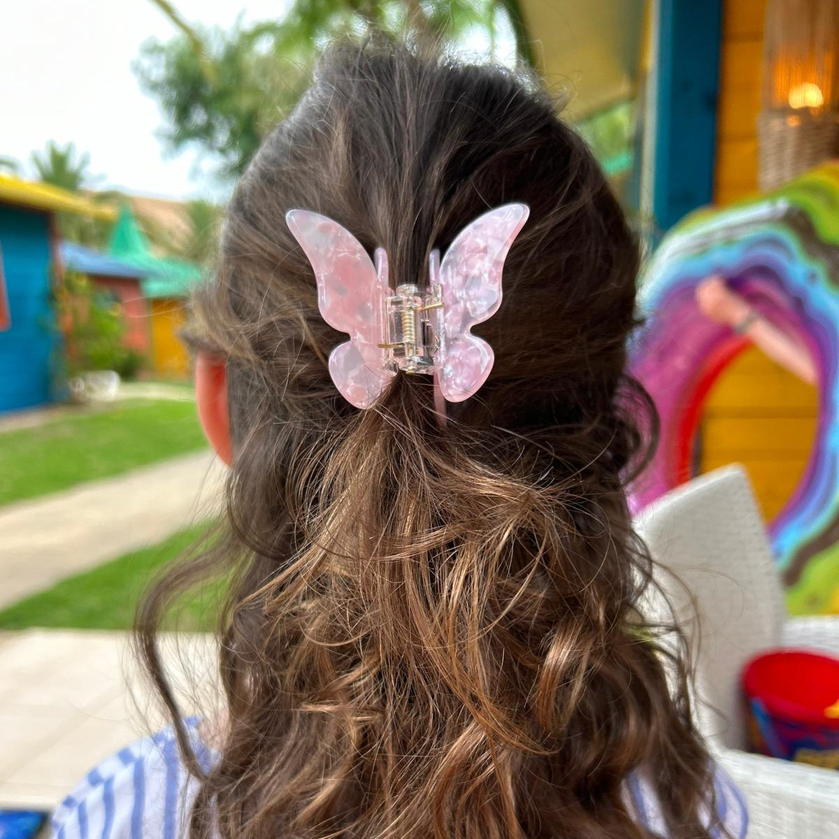 Person with wavy hair wearing a pink butterfly hair clip in an outdoor setting