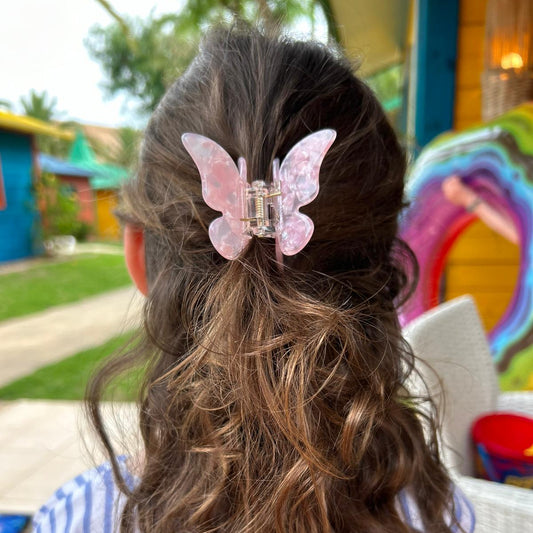 Person with wavy hair wearing a pink butterfly hair clip in an outdoor setting